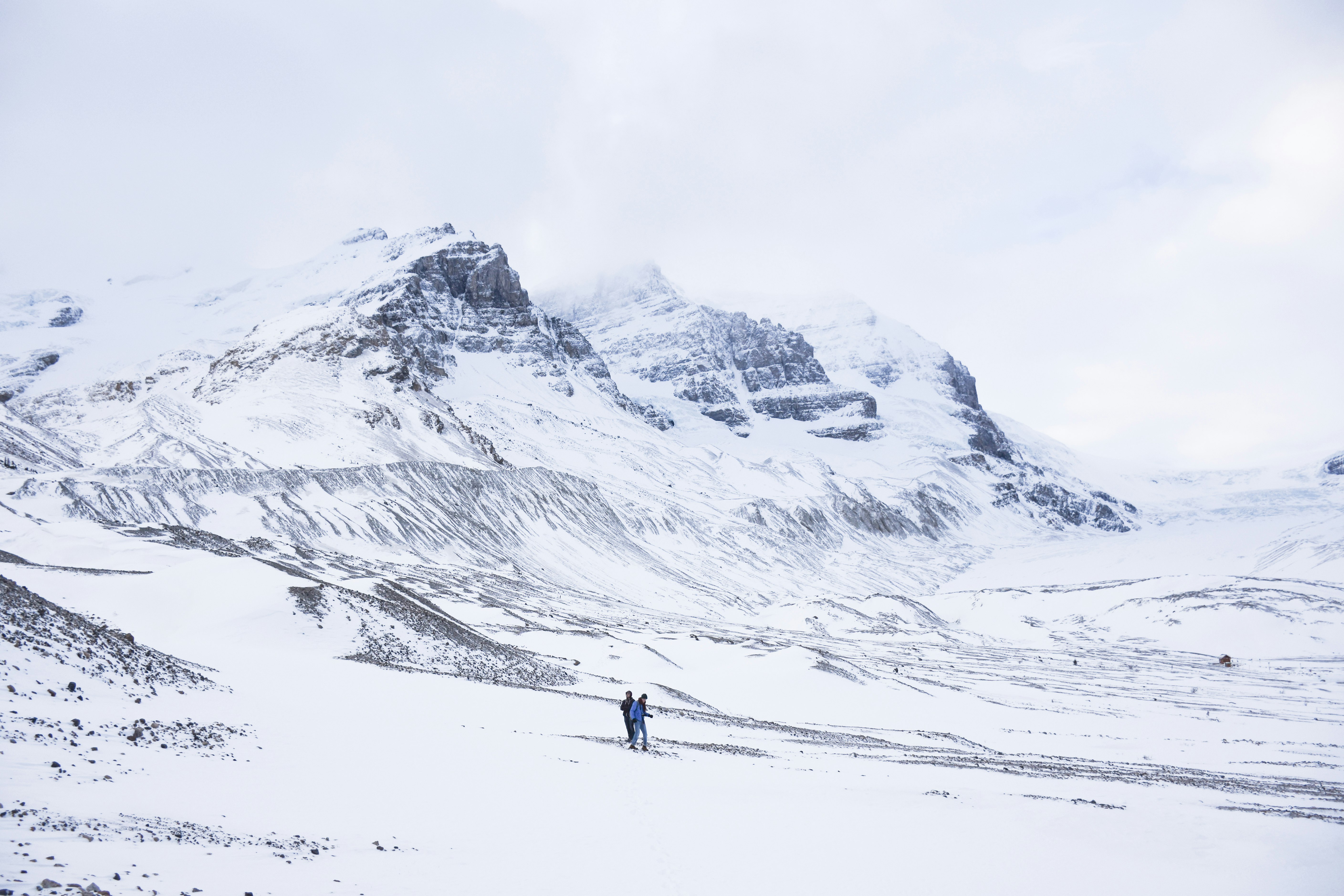 two person walking on snow covered ground next to mountains